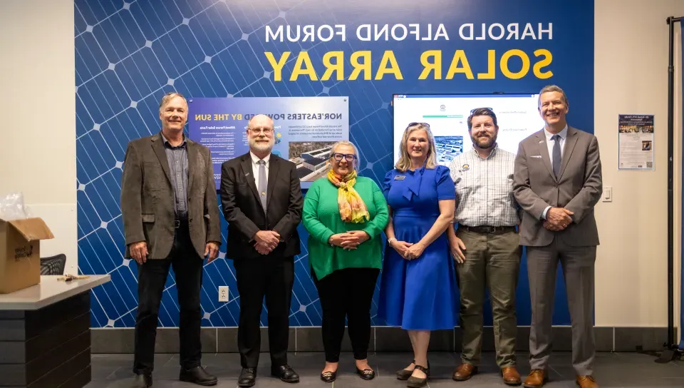 A group of UNE administrators poses in front of a mural 